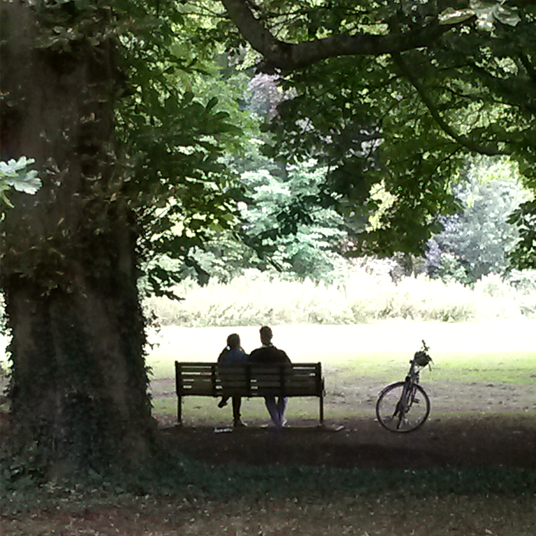 A couple sat on a park bench in an open space in Cambridge.